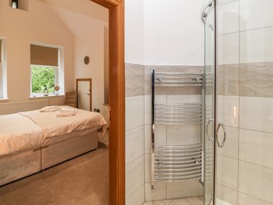 A bedroom with a bed near windows and a connected bathroom with a glass shower enclosure and a chrome towel rail at On the Straits in Glyngarth near Menai Bridge