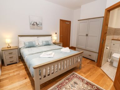 A bedroom with double bed bedside tables lamps wardrobe and an ensuite bathroom at On the Straits in Glyngarth near Menai Bridge
