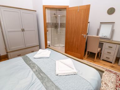 A bedroom with a bed with folded towels a wardrobe a desk with a chair and a mirror and an open door showing a shower at On the Straits in Glyngarth near Menai Bridge