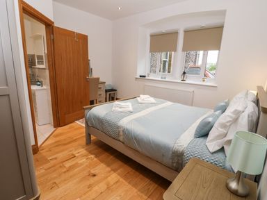 A bedroom with a double bed, bedside table with lamp, window with blinds, and an open door leading to a bathroom at On the Straits in Glyngarth near Menai Bridge
