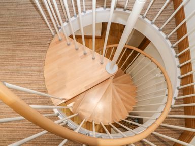 A wooden spiral staircase with white railings and beige carpeted floor at On the Straits in Glyngarth near Menai Bridge