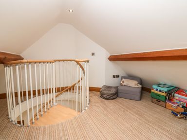A small carpeted attic space with a spiral staircase a small chair and a stack of board games at On the Straits in Glyngarth near Menai Bridge