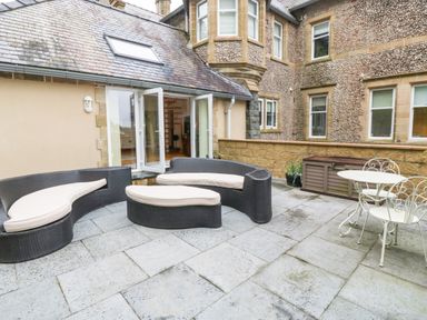 A patio with a curved outdoor sofa set and a round metal table with chairs at On the Straits in Glyngarth near Menai Bridge