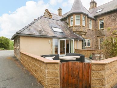 An outdoor patio with seating and a wooden gate outside a stone and stucco house at On the Straits in Glyngarth near Menai Bridge