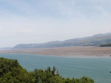 A coastal view with green trees in the foreground blue water and hills in the background at On the Straits in Glyngarth near Menai Bridge