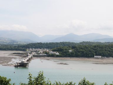 A coastal view with a long pier leading to a small town surrounded by trees and mountains at On the Straits in Glyngarth near Menai Bridge