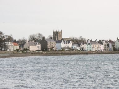 A row of houses by the water with a church tower behind them in Beaumaris