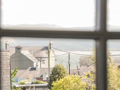 A view through a window showing rooftops, utility poles, water, and distant hills at Gwel Y Mor in Beaumaris