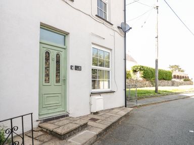 The exterior of a house with a light green door and a window on a paved sidewalk at Gwel Y Mor in Beaumaris