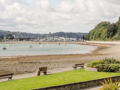 A beach with boats on the water and benches near a grassy area with shrubs at Gwel Y Mor in Beaumaris