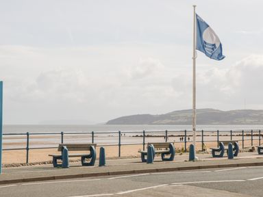 Benches along a pavement by the beach with a flagpole and sea in the background at Gwel Y Mor in Beaumaris