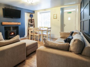A living room with beige sofas wooden dining table with six chairs a fireplace and a wall-mounted television at Gwel Y Mor in Beaumaris