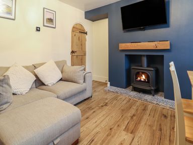 A living room with a beige sofa, a wood-burning stove in a blue fireplace, a mounted TV, and a wooden door at Gwel Y Mor in Beaumaris