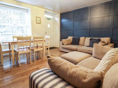 A living room with beige sofas and a dining table with chairs near a window at Gwel Y Mor in Beaumaris