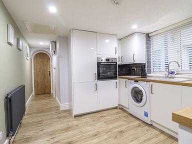 A kitchen with white cabinets a washing machine an oven a microwave and a wooden door at Gwel Y Mor in Beaumaris