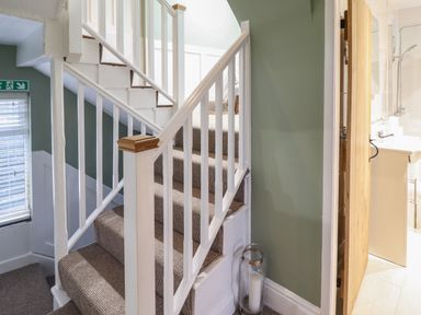 A carpeted staircase with white railings next to a light green wall and an open wooden door leading to a bathroom with a sink