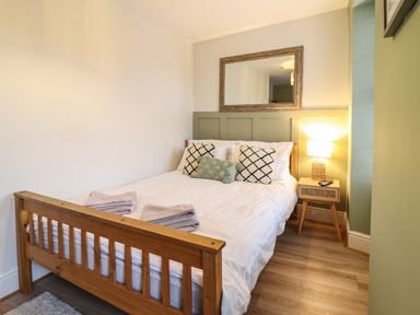A bedroom with a wooden bed, white bedding, pillows, a bedside table with a lamp and a remote at Gwel Y Mor in Beaumaris