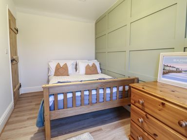 A bedroom with a wooden bed with pillows and a chest of drawers with a framed picture at Gwel Y Mor in Beaumaris