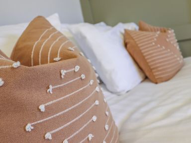 Two brown decorative pillows with white stitched patterns on a white bed with white pillows at Gwel Y Mor in Beaumaris