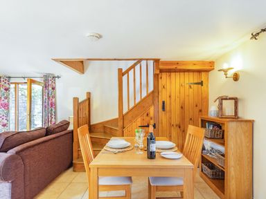 A dining area with a wooden table set for two next to a wooden staircase and a bookshelf at Millers Lodge in St Keyne near Liskeard