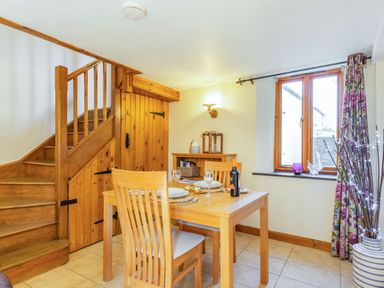 A dining area with a wooden table and chairs next to stairs and a window at Miller's Lodge in St Keyne near Liskeard
