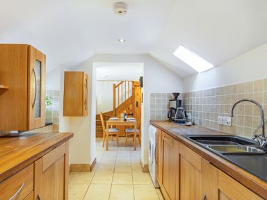 A kitchen with wooden cabinets a sink coffee maker and a dining table with chairs in the background at Millers Lodge in St Keyne near Liskeard