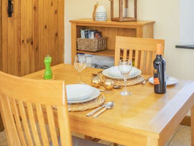 A wooden dining table set with plates glasses cutlery a green pepper grinder and a bottle of wine at Miller's Lodge in St Keyne near Liskeard