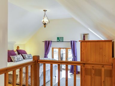 A bedroom with a bed purple pillows purple curtains a wooden dresser and a wooden railing at Miller's Lodge in St Keyne near Liskeard