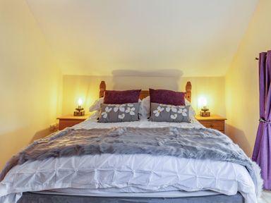 A bedroom with a bed with pillows and a throw with lamps on bedside tables at Millers Lodge in St Keyne near Liskeard