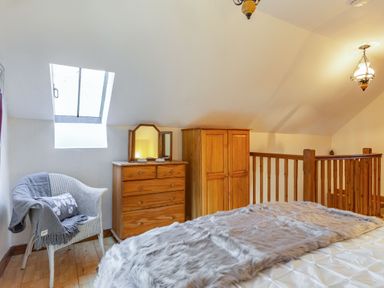 A bedroom with a bed covered by a furry blanket a wooden dresser with a mirror a wooden wardrobe a wicker chair with a blanket and cushion and a skylight window at Miller's Lodge in St Keyne near Liskeard