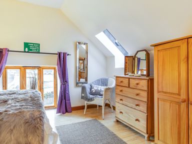 A bedroom with a bed covered in a fur blanket a wicker chair beside a dresser and wardrobe with a skylight window at Millers Lodge in St Keyne near Liskeard