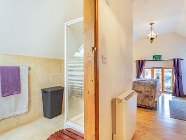 A bathroom with a shower and towels next to a bedroom with a bed and curtains at Miller's Lodge in St Keyne near Liskeard