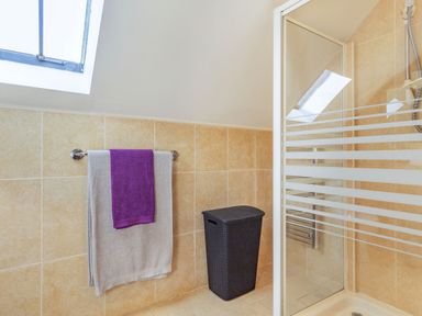A bathroom with a shower area a black laundry basket and two towels hanging on a rail at Millers Lodge in St Keyne near Liskeard