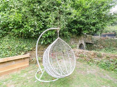 A hanging garden chair in a yard with ivy and stone walls at Millers Lodge in St Keyne near Liskeard