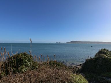 A coastal view showing the sea with vegetation and hills in the background at Sandpiper in Weymouth
