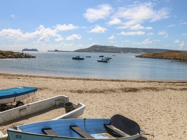 A sandy beach with small boats on the shore and boats floating on water at Sandpiper in Weymouth