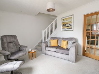 A living room with a gray sofa with cushions a recliner chair a small wooden table stairs and a wooden door with glass panels at Sandpiper in Weymouth