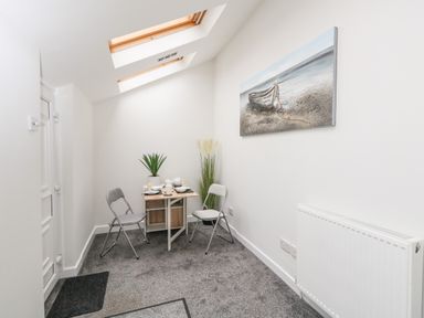 A small dining area with a table set for two folding chairs a plant painting radiator and skylight windows at Sandpiper in Weymouth