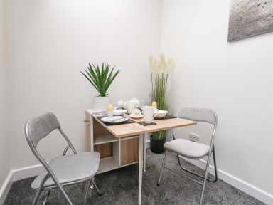 A small dining area with a wooden table set for two with plates and mugs two folding chairs and potted plants at Sandpiper in Weymouth