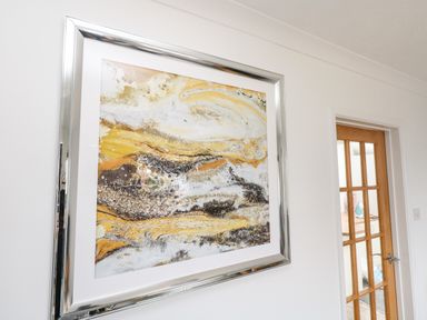 A wall with an abstract painting in a silver frame next to a wooden door with glass panels at Sandpiper in Weymouth