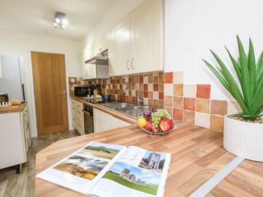 A kitchen with wooden countertops a fruit bowl an open book a plant and appliances at Sandpiper in Weymouth