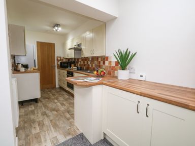 A kitchen with wooden countertops tiled backsplash and wooden door at Sandpiper in Weymouth