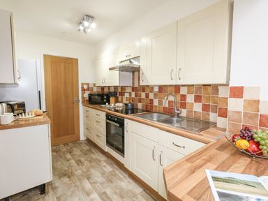 A kitchen with wood countertops white cabinets tiled backsplash and a wooden door at Sandpiper in Weymouth