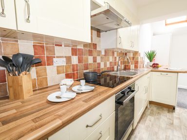 A kitchen with wooden countertops, a stove, sink, white cabinets, utensils in a holder, and tiled backsplash at Sandpiper in Weymouth