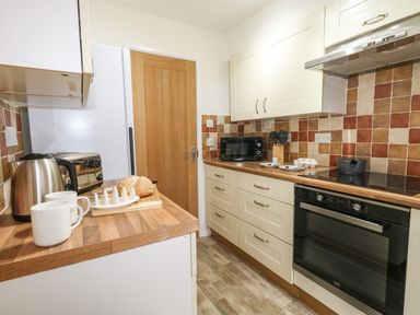 A kitchen with wooden countertops and cabinets a microwave oven kettle toaster and a loaf of bread at Sandpiper Weymouth