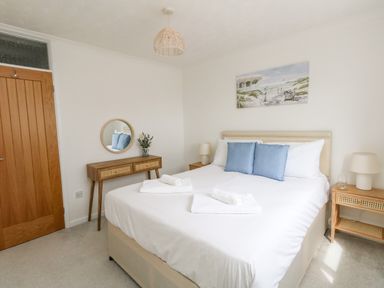 A bedroom with a bed with blue pillows towels on it bedside tables lamps and a wooden door at Sandpiper in Weymouth