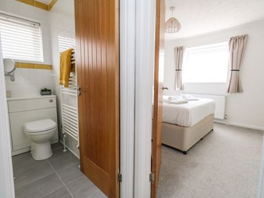 A bathroom with a toilet and towel rail next to a bedroom with a bed and window at Sandpiper in Weymouth