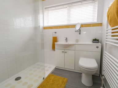 A bathroom with a shower, toilet, sink, and yellow towels at Sandpiper in Weymouth