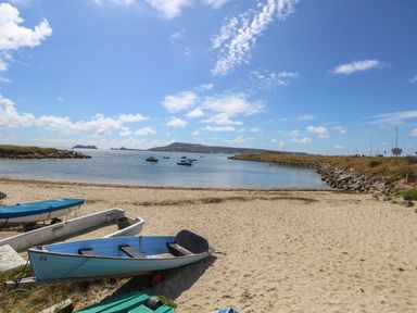A sandy beach with small boats on the shore and more boats in the water at Sandpiper in Weymouth