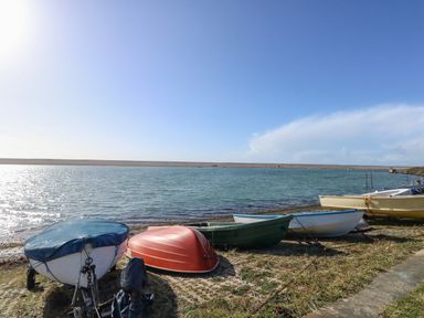 Several small boats on the shore next to a body of water under a clear sky at Sandpiper in Weymouth